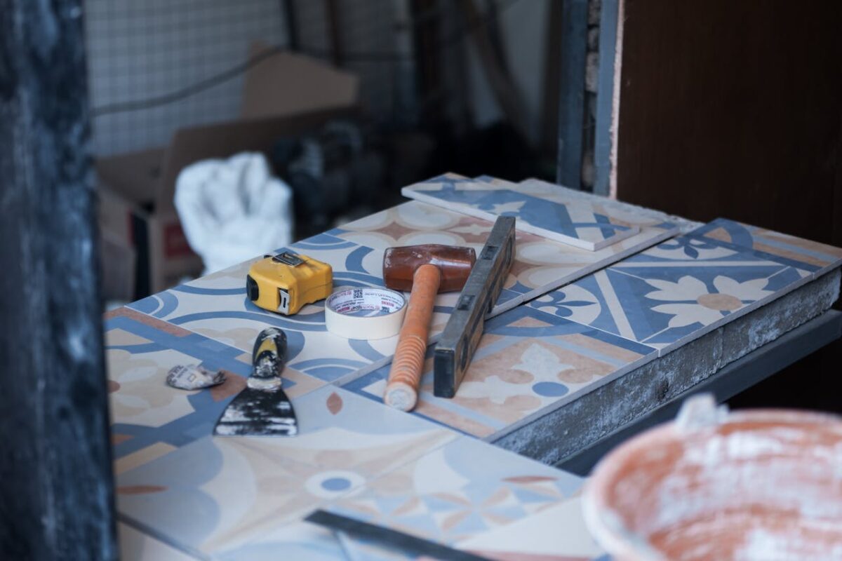who-we-are Tools and tiles on a construction site, ready for tiling work. Includes trowel, tape measure, and adhesive tape.