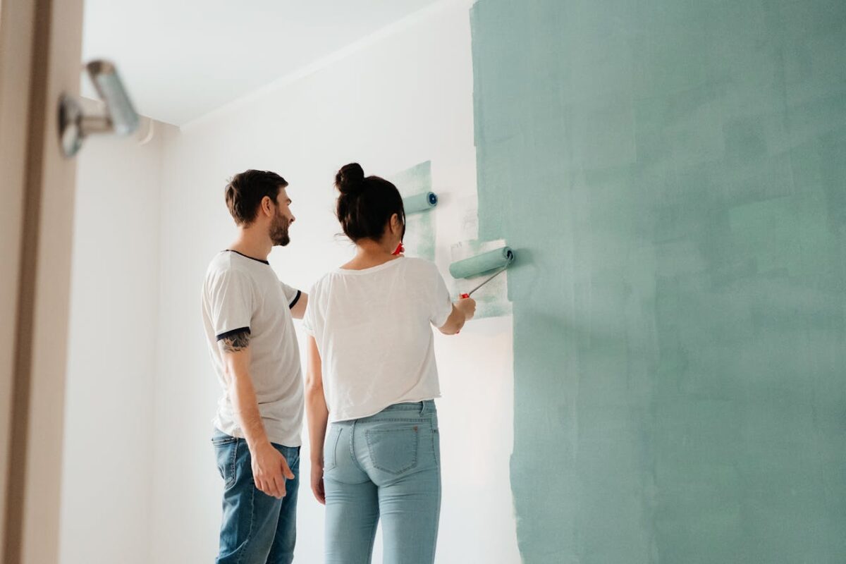 services-04 A couple collaborates to paint a wall with a roller indoors, showcasing teamwork.